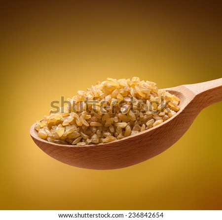 Bulgur in a wooden spoon / cereal on wooden spoons isolated on golden background
