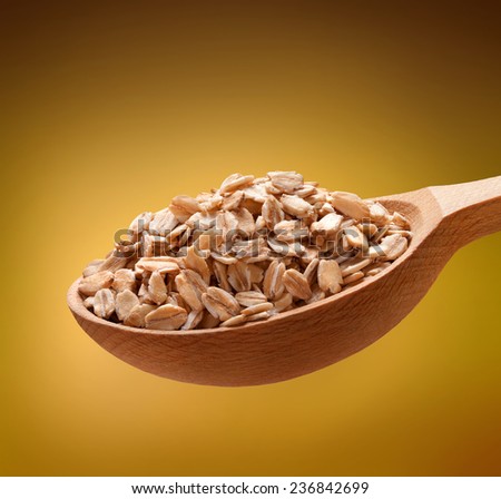 Rolled oats in a wooden spoon / cereal on wooden spoons isolated on golden background