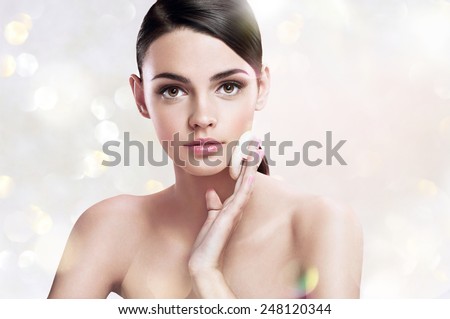 Young woman applying powdered foundation on her face with cosmetic sponge puff, skin care concept / photoset of attractive brunette girl on blurred background with bokeh