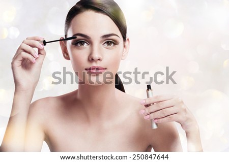 Charming young woman applying mascara / photoset of attractive brunette girl on blurred background with bokeh