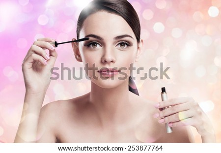 Charming young lady applying mascara / photoset of attractive brunette girl on blurred pink background with bokeh