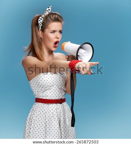 Formidable pin-up girl shouting into a megaphone, mouthpiece, speaking trumpet. Film-making or film production concept / photo set of young American pin-up model on blue background