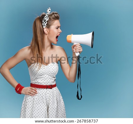 Nervous pin-up girl screaming with megaphone, mouthpiece, speaking trumpet. Film-making or film production concept / photo set of young American pin-up model on blue background