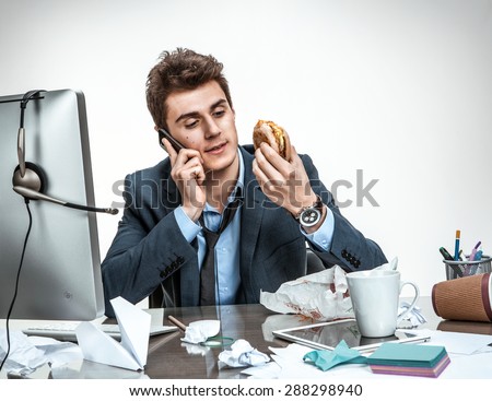 Slacker man talking on the phone while eating at work / modern office man at working place, sloth and laziness concept