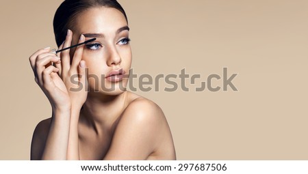 Mascara applying. Makeup closeup. Eyes make-up / photos of appealing brunette girl on beige background