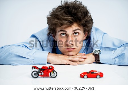 Pensive young guy give rein to his imagination / photos of young man resting his chin on his hands, laying on a table and looking upwards over gray background