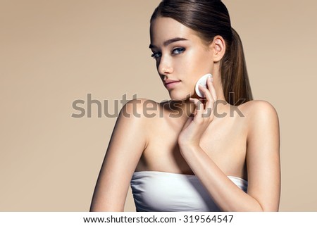 Beautiful brunette woman removing makeup from her face, skin care concept / photo composition of brunette girl with beige background