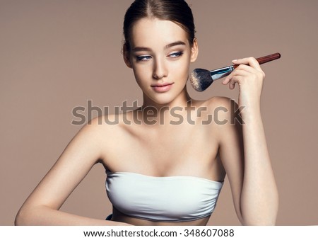Beautiful teenage girl applying cosmetic powder on her face with tassel, skin care concept / photoset of attractive brunette girl on beige background