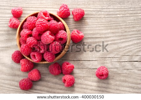 Ripe sweet raspberries in bowl on wooden table. Close up, top view, high resolution product