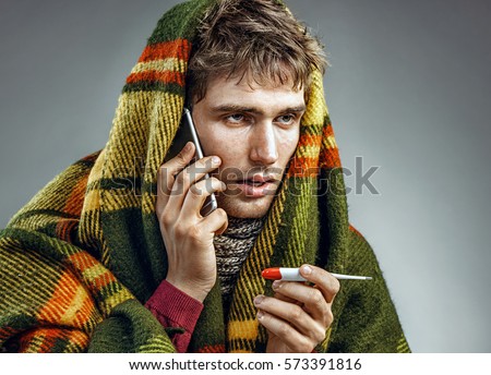 Sick man wrapped in blanket with a high temperature calling on the phone. Man suffering cold and winter flu virus. Health care concept
