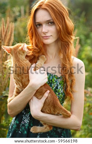 Natural beautiful red-haired girl holds on hands of a red-haired cat, kitten