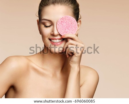 Funny girl holding pink sponge near her face. Portrait of young girl on beige background. Youth and skin care concept