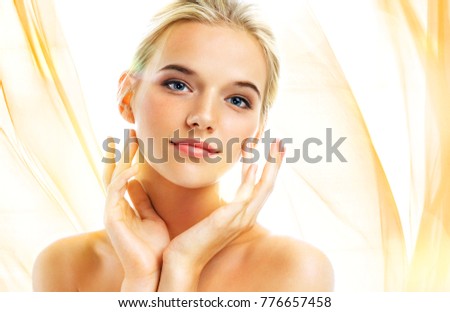 Attractive young girl touching her face on wavy orange background. Youth and skin care concept