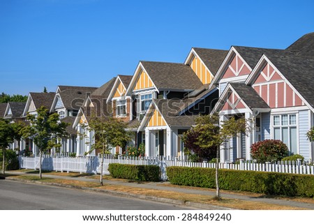 A row of a new houses in Richmond, British Columbia, Canada. Front yards of the houses and street with trees and bushes.