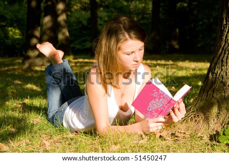 The young girl lies on a grass and reads the book