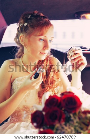 The bride sitting in the wedding car with lipstick and a pocket mirror in hands