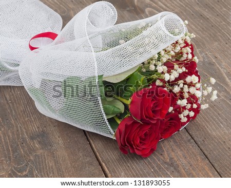 Red roses and white flowers wrapped in white on a wooden  background.
