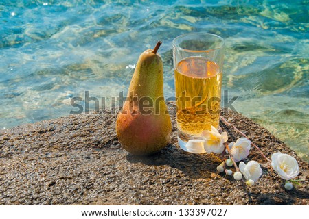 Pear juice in a glass, pear and flowers on a background of the sea.