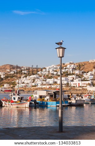 Fishing boats in the harbor town of Mykonos at sunset and seagull on street lights