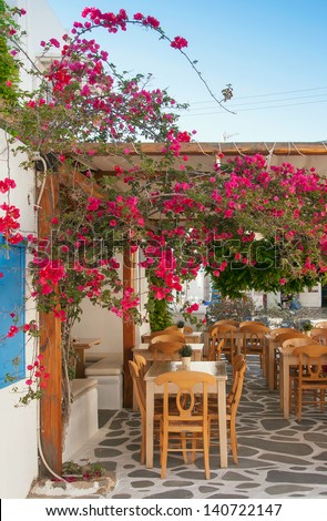 Restaurant on the narrow street of the island in Greece with tables and shrubs flowers