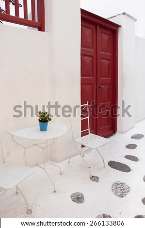 Red wooden door and cafe tables in the narrow streets of Mykonos.