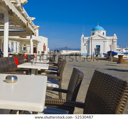 Tables and chairs for the restaurant on the seafront of Mykonos on the background of the church