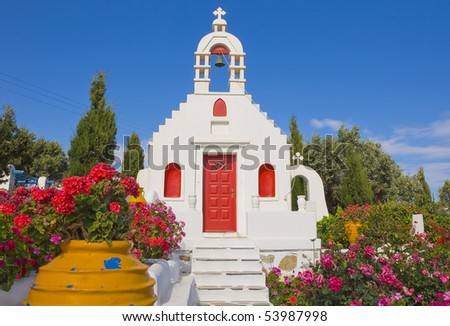 Classical Greek architecture of the churches on the islands. White Church, surrounded by flowers in the garden and colorful pots ...