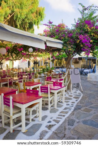 Restaurant on the narrow street of the island in Greece with colored tables and shrubs flowers
