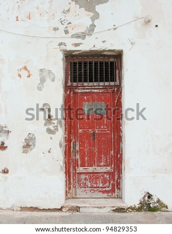 Old red door with bars on the white building. Background.