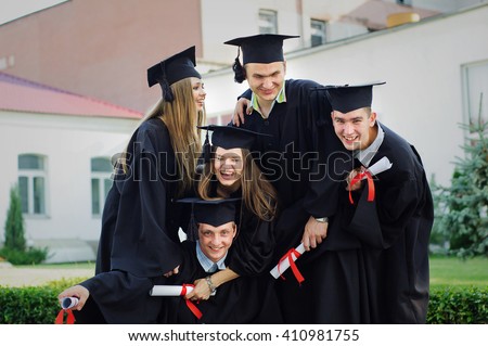 Graduates embrace, enjoy and look at the camera on the graduation ceremony. Happy graduation day. 5 graduates hold his graduate diplomas in their hands.