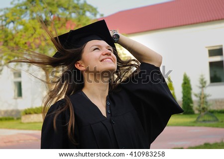 A graduate in the mantle looks up and thinks of a great future. Beautiful graduate girl with flying hair and graduate cap.