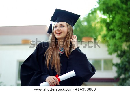 A beautiful graduate girl in the mantle keeps in hands graduation diploma and looks up.