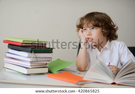 A child of primary school age do homework. The boy does his homework at his desk at home. The student / pupil has been bored on the lesson.