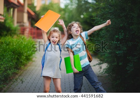 Boy and girl rejoice to the termination of academic year. They have raised hands and pose ridiculous mugs. Behind the back of everyone satchel. Back to school.  Little first graders.