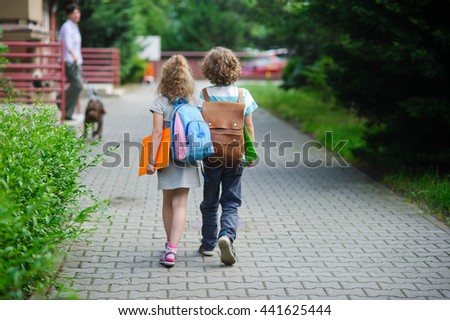 Two pupils of primary school go hand in hand. Boy and girl with school bags behind the back. Beginning of school lessons. Warm day of fall. Back to school.  Little first graders.