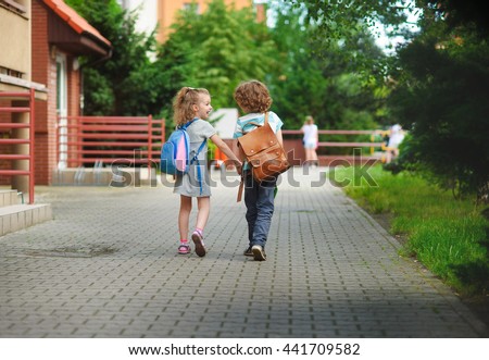 Boy and girlie go to school having joined hands. Warm September day. Good mood. Behind backs at children satchels. The girlie laughs. Back to school.  Little first grader.