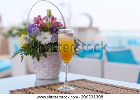 Alcoholic drink with fruit juice in glass. Blur beautiful bouquet of flowers.