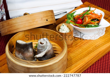 tableware, wood cup with steamed fish, salad, cutlery. Creative cuisine.