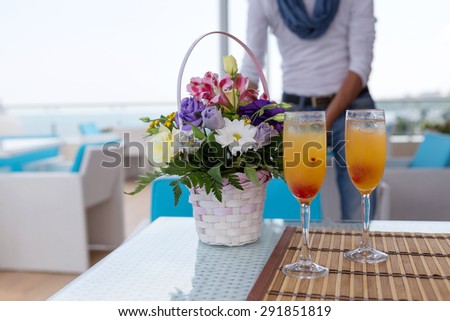 Alcoholic drink with fruit juice in glass. Blur beautiful bouquet of flowers. Soft selective focus.