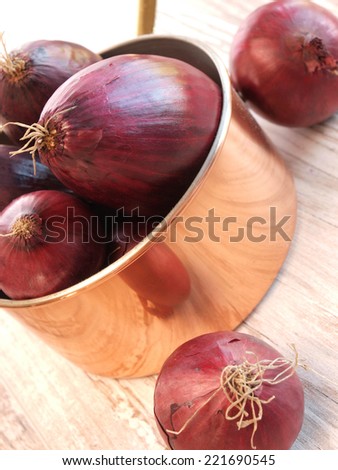 Red onions in a copper pan on a rustic wooden background