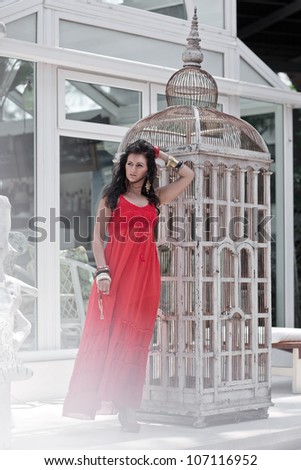 beautiful woman in red dress standing near the vintage high cage