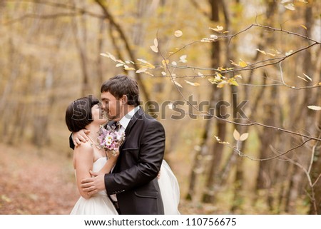 Kissing bride and groom in their wedding day near autumn tree in the forest