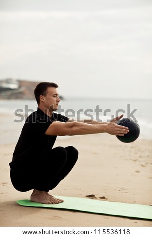 muscular man does body exercises with a ball near the ocean