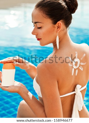 Girl putting sun block near pool holding white sun tan lotion