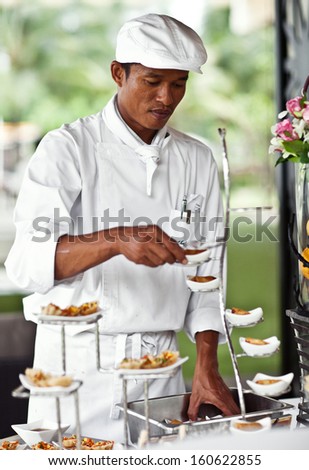 Asian chef laying a table with luxury food and drinks on wedding.
