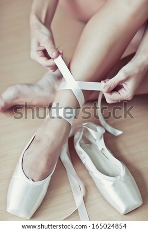 Ballet dancer tying slippers around her ankle woman ballerina pointe