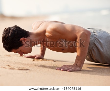 fitness man exercising push ups. Male fitness model cross-training on beach. Caucasian man in his twenties.