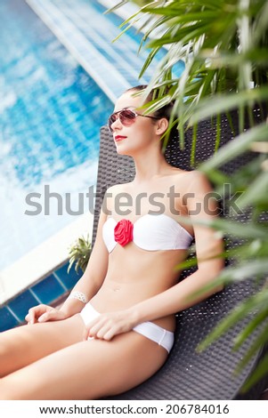 Woman in bikini relaxing in deck chair by pool