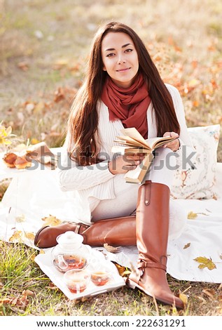 young beautiful brunette drink tea and read book in the autumn park
