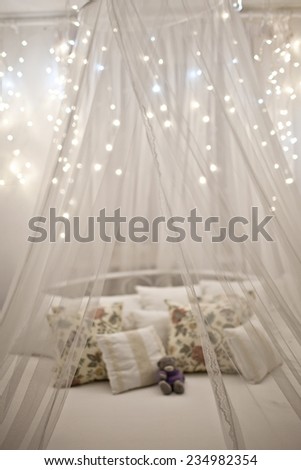 White cozy bed with vintage pillow and Christmas lights, defocused